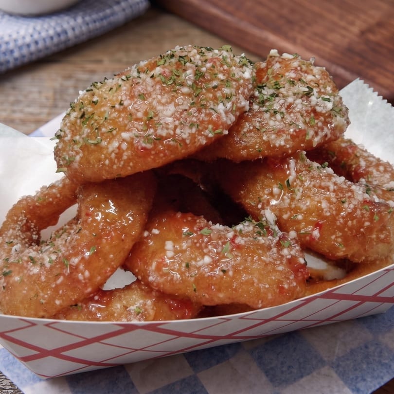 Sweet and savory onion rings, glazed with honey garlic sauce and sprinkled with parsley, in a paper tray.