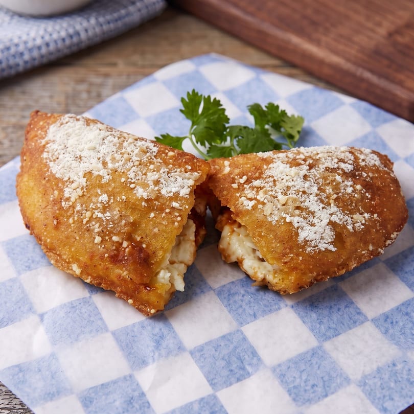 Golden-brown fried calzone, split open to reveal melted cheese and sauce, on blue and white checkered paper.