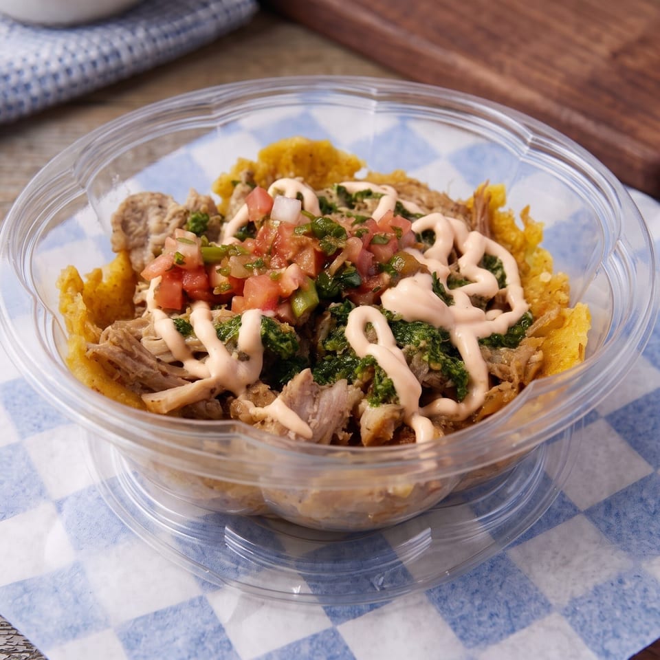 A clear plastic bowl filled with shredded meat, salsa, green sauce, and a creamy drizzle.